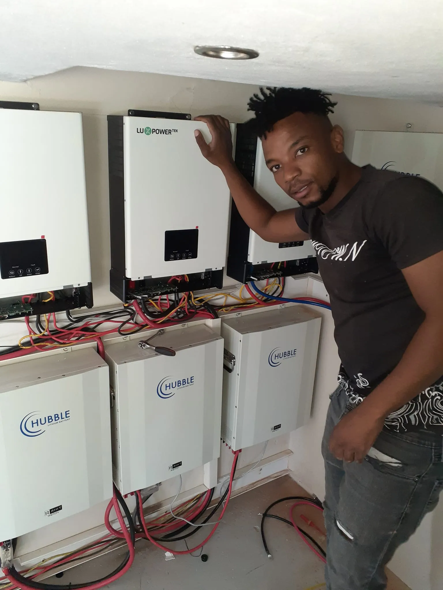 A Magana Power Solutions technician next to a completed installation of wall-mounted inverters and lithium battery storage
